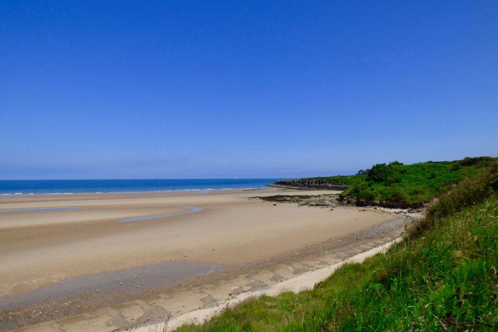 A view of Lligwy beach on a sunny day with golden sand and blue sea.